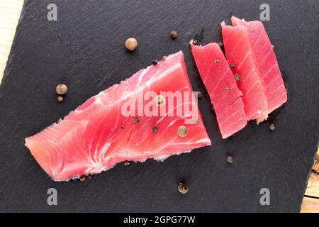 Un pezzo di tonno leggermente salato su una pietra ardesia, primo piano, vista dall'alto. Foto Stock