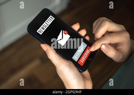 Mano di femmina che usa il telefono cellulare per iscriversi alla newsletter. Email marketing e newsletter, comunicazione e informazioni sui clienti Foto Stock