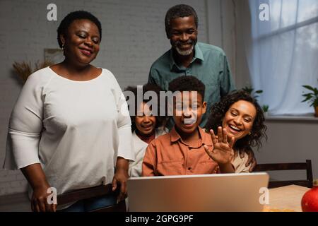 eccitato ragazzo afroamericano che agita la mano durante la videochiamata vicino alla famiglia Foto Stock