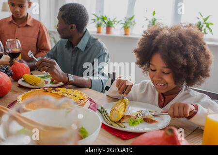 ragazza afroamericana che ha cena di ringraziamento vicino al nonno blurred e fratello Foto Stock