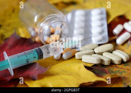 Siringa e pillole sulle foglie d'acero autunnali. Assistenza sanitaria durante la stagione di raffreddore e influenza Foto Stock