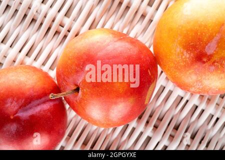 Tre succose prugne rosse-gialle su un tappeto di vite, primo piano, vista dall'alto. Foto Stock