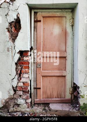 Porta anteriore in legno grigio shabby con pannello di vetro e griglie in metallo in un vecchio muro di pietra Foto Stock