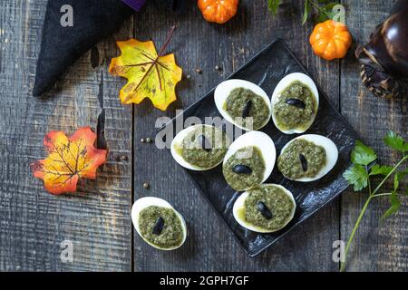 Halloween divertente idea per il cibo partito. Halloween uova farcite creative con salsa di pesto su un tavolo di legno. Vista dall'alto sfondo piatto. Foto Stock