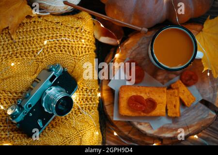 Vista dall'alto della composizione delle feste. Il concetto di Ringraziamento. Cacao, torta di carote, albicocche secche su un vassoio di legno maglione Knit, una macchina fotografica vintage, zucca rotonda, garland e foglie di giallo autunno. Foto Stock