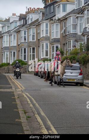 Motociclista in attesa di passare Un Cavallo e Rider su una strada stretta con le automobili parcheggiate Foto Stock