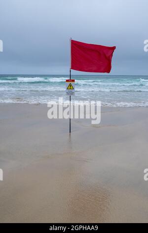 Una bandiera di avvertimento rossa del bagnino (con il segno di avvertimento) su Una spiaggia della Cornish Foto Stock