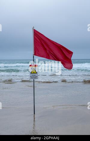 Una bandiera di avvertimento rossa del bagnino (con il segno di avvertimento) su Una spiaggia della Cornish Foto Stock