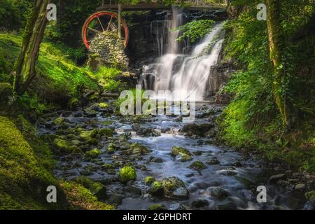 Ruscello che conduce alla ruota d'acqua rossa e cascata nel Glenareff Forest Park, County Antrim, Irlanda del Nord. Foto a lunga esposizione e messa a fuoco morbida Foto Stock