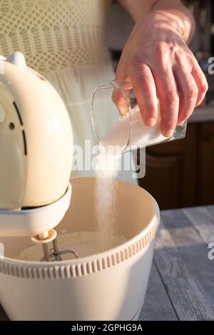 Passo dopo passo il processo di produzione della panna acida. Le mani delle donne aggiungono lo zucchero al recipiente del mixer con la panna acida. Foto Stock