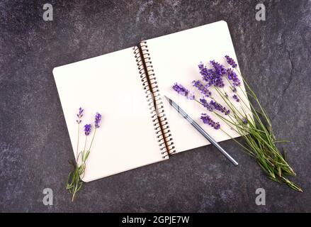 Vista dall'alto del blocco note vuoto aperto con bouquet di lavanda su sfondo di pietra nera, spazio di copia per il testo Foto Stock