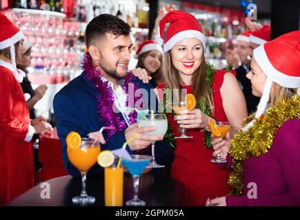 Uomo e due donne con cocktail a Babbo Natale cappelli festeggiamenti al nightclub Foto Stock