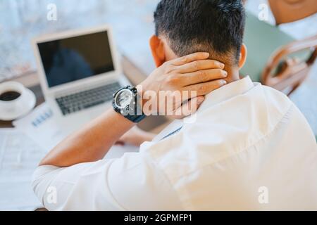 Uomo d'affari doloroso collo mentre seduto sul divano sul posto di lavoro. Concetto di sindrome da ufficio. Foto Stock