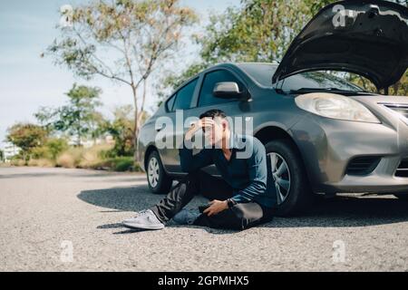 Grave mal di testa uomo seduto accanto a guasto auto su strada. Concetto di auto rotta. Foto Stock