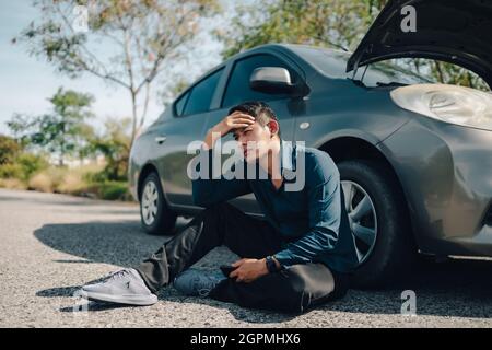 Grave mal di testa uomo seduto accanto a guasto auto su strada. Concetto di auto rotta. Foto Stock