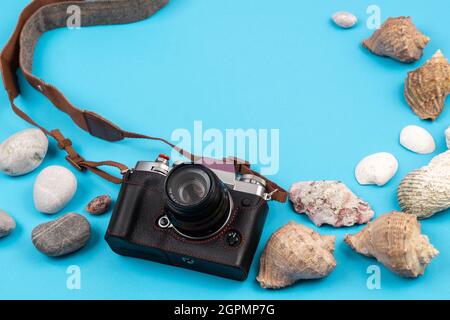 Macchina fotografica e conchiglie su sfondo blu.sfondo per il viaggiatore. Foto Stock