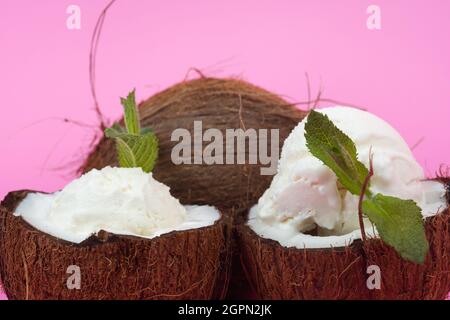 Palline di gelato alla vaniglia in semi di cocco fresco decorate con foglie di menta su sfondo rosa. Foto Stock