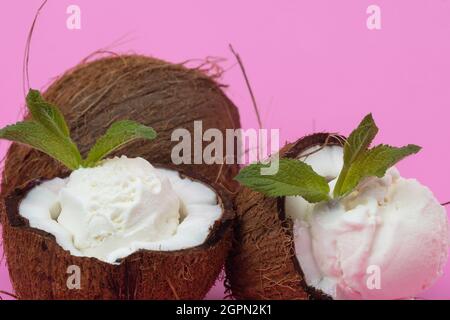 Palline di gelato alla vaniglia in semi di cocco fresco decorate con foglie di menta su sfondo rosa. Foto Stock