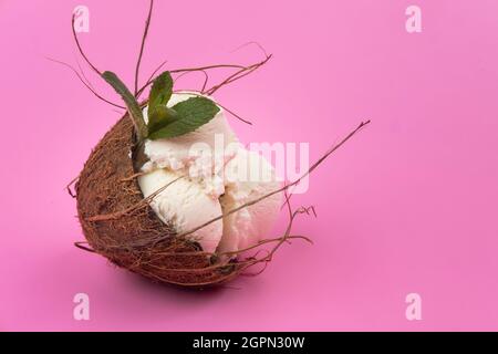 Palline di gelato alla vaniglia in un cocco vuoto decorato con foglie di menta su sfondo rosa. Foto Stock