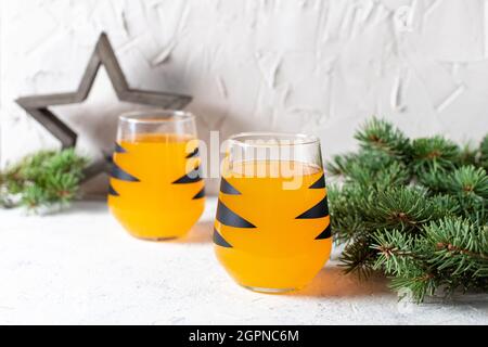 cocktail mandarino arancione in vetro con strisce nere. Drink di benvenuto per le feste di Natale. Concetto per bambini anno nuovo con rami di albero Foto Stock