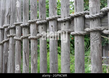 Vecchia recinzione rustica in legno resistente agli agenti atmosferici fissata con corda pesante spessa Foto Stock
