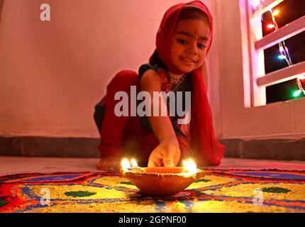 Una bambina ha messo una lampada di terra sul pavimento decorato della sua casa in occasione del festival Diwali a Nuova Delhi. Foto Stock