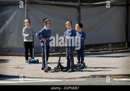 I ragazzi ebrei asidici sui loro scooter aspettano che una luce cambi su Bedford Avenue a Williamsburg, Brooklyn, New York. Foto Stock