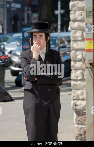 Un uomo ebreo ortodosso pensivo attende ad un angolo di strada su Lee Avenue a Williamsburg, Brooklyn, New York City. Foto Stock