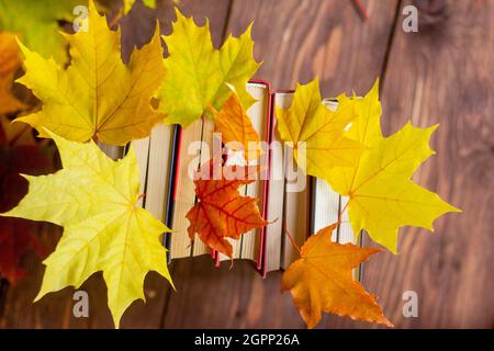 Una pila di libri con brillante autunno lascia tra le pagine su una tavola rustica in legno Foto Stock