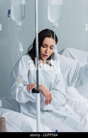 donna malata che guarda il catetere durante la terapia in ospedale Foto Stock