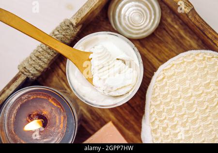 Bodywhip noto anche come burro corpo, crema idratante per la cura della pelle su cucchiaio di legno e vasetto su vassoio di legno naturale con spugna da bagno e candela. Foto Stock