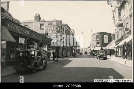 High Street, Ramsgate, Thanet, Kent, c1945-c1965. Una vista sulla strada di High Street, guardando a nord-ovest con negozi su entrambi i lati e no. 113 sullo sfondo su un bivio con Chatham StreetIl negozio in primo piano sulla destra ha legno-incorniciato secondo piano con maniglioni e finestre con getti. Di fronte si trova un negozio chiamato 'E.J. Bella &amp; Son' e un grande cartello per 'Nestle's Milk' su un edificio più in alto con una baia d'angolo cementata. N0. 113 ha un frontale curvo con finestre cieche alternate Foto Stock