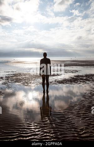 Il sole tramonta una scultura Antony Gormley Iron Man sulla spiaggia di Crosby, Merseyside 'un altro posto' con la bassa marea Foto Stock