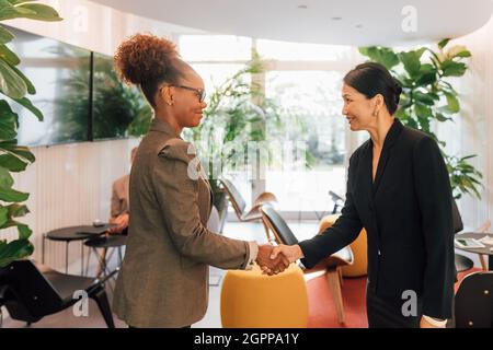 Italia, donne d'affari sorridenti che scuotono le mani in uno studio creativo Foto Stock