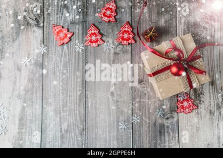 Scatola regalo di Natale e giocattoli di Natale rossi su sfondo di legno con fiocchi di neve e bagliori. Foto Stock