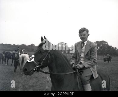 Anni '50, storico, fuori in un campo in un evento equestre, un giovane adulto maschio pilota in una giacca e cravatta seduta sul suo cavallo, West Sussex, Inghilterra, Regno Unito. Foto Stock