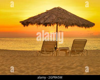 Ombrellone e sdraio in paglia su una costa di sabbia ideale al tramonto Foto Stock