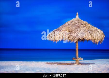 Ombrello di paglia su una idilliaca costa sabbiosa con cielo blu e mare sullo sfondo Foto Stock