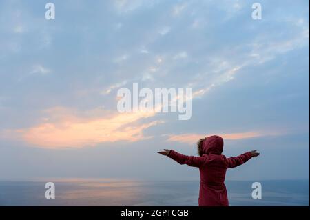 La signora con le braccia tese verso il mare Foto Stock