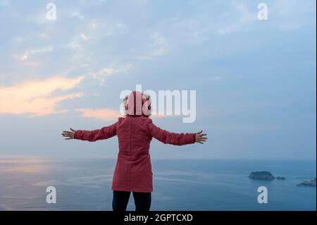 La signora con le braccia tese verso il mare Foto Stock