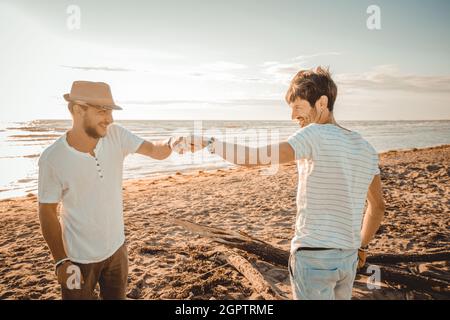 Due ragazzi caucasici sorridenti sulla spiaggia si salutano con un tocco di pugno - incontra il concetto, mostrando rispetto e amicizia avendo buone relazioni Foto Stock