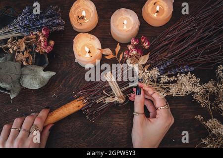 Wiccan Witch che decorano una scopa autoctinata per la celebrazione del Samhain. Scopa fatta a mano su un tavolo di legno scuro Foto Stock