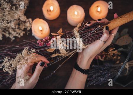 Wiccan Witch che decorano una scopa autoctinata per la celebrazione del Samhain. Scopa fatta a mano su un tavolo di legno scuro Foto Stock