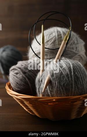 Ciotola in vimini con palle di filato e aghi da maglieria su fondo di legno Foto Stock