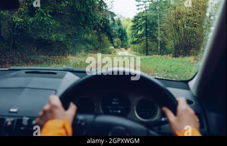 Autista vestito giacca arancione brillante guida una moderna fuoristrada guida a destra RHD auto sulla montagna verde foresta di campagna strada. POV all'interno dei venti auto Foto Stock