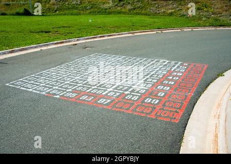 Un colorato gioco di divertimento per bambini all'aperto di serpenti e scale a forma di una piazza. Ci sono numeri tra uno e cento Foto Stock