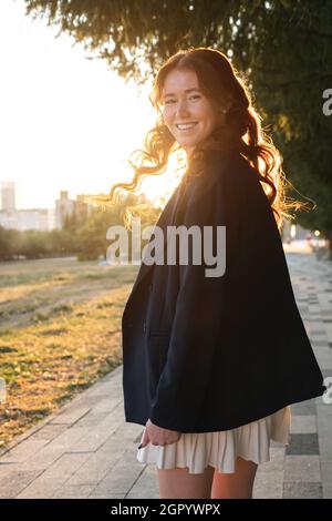 Bella signora si gira indietro scuotendo i capelli a piedi lungo la strada del parco Foto Stock