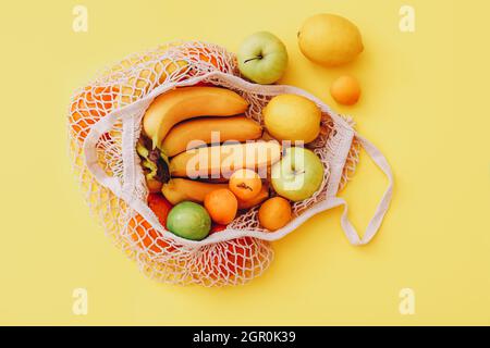 Borsa in maglia di cotone con frutta fresca colorata su sfondo giallo, vista dall'alto. Concetto di zero rifiuti Foto Stock