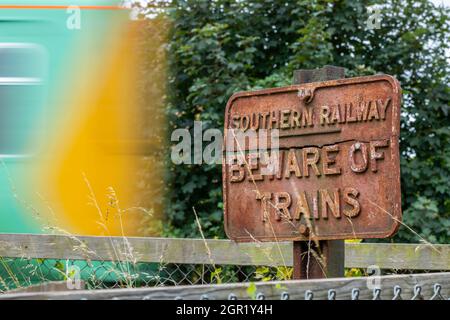 vintage Southern Railway cartello in ghisa attenzione ai treni con un treno veloce sfocato nella livrea ferroviaria meridionale che passa a velocità. southern Railway TOC. Foto Stock