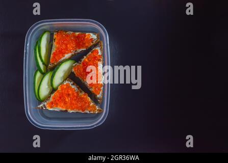 Pranzo di Capodanno a lavorare in una scatola trasparente con sandwich caviale rosso e cetrioli freschi su sfondo nero. Foto di alta qualità Foto Stock